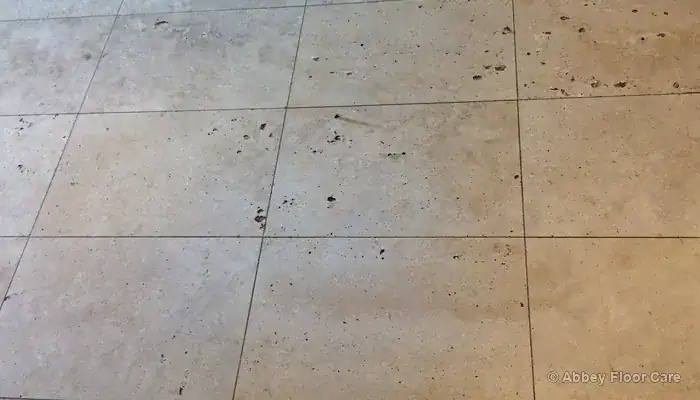 Dirty travertine floor with dark soil trapped in natural holes and recessed grout lines