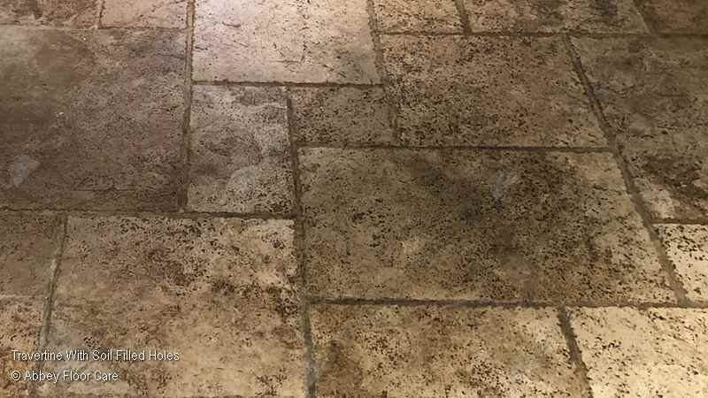 Dirty travertine floor with compacted soil lodged in open holes and natural voids