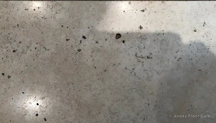 Worn travertine tile with dull patches, exposed pits and fine surface scratches